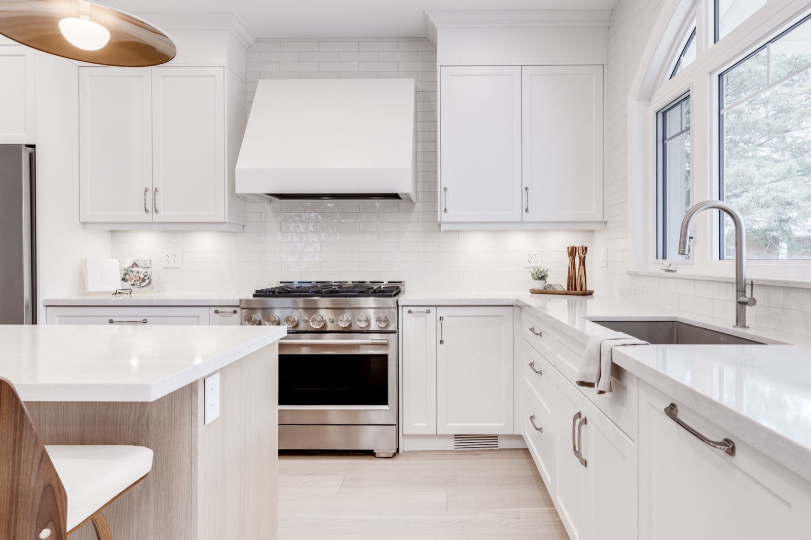 Bright white kitchen with quartz counters, shaker cabinets, island seating and a window over the sink.