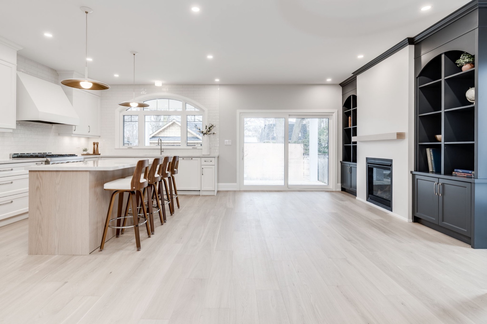 Open-concept Toronto kitchen with warm white cabinetry, oak island, charcoal built-ins and pale wood flooring.