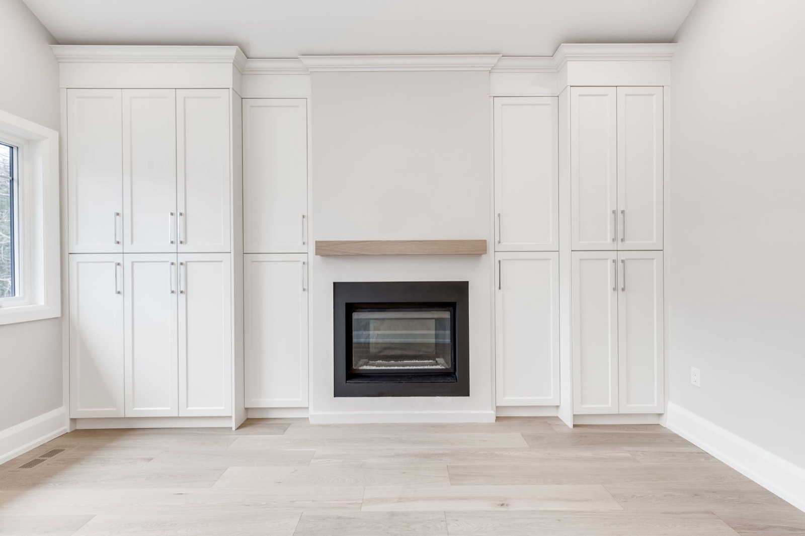 Bright living room with white built-ins, a black gas fireplace, oak mantel and pale hardwood flooring.