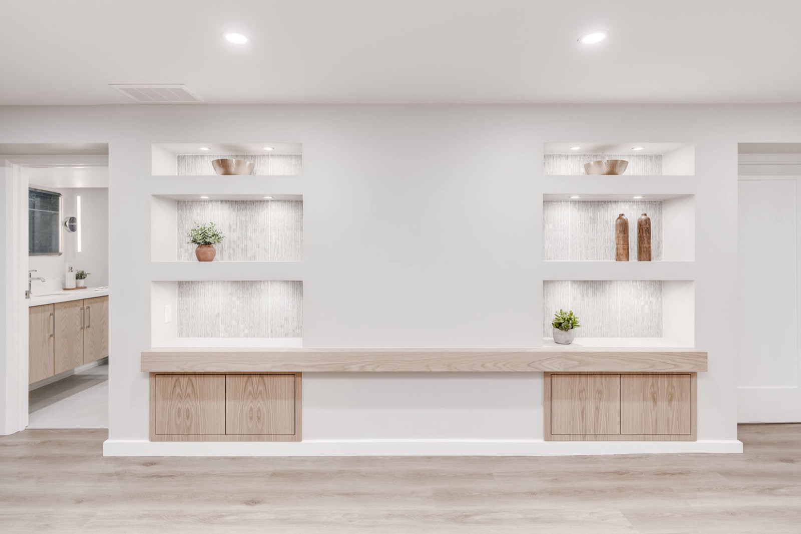 Finished basement media wall with white built-ins, natural oak cabinetry, and recessed lighting.